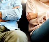 Close up of divorcing man and woman sitting on a sofa with their arms crossed.