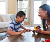 The young boy with Down Syndrome enjoys play therapy with his therapist at home.