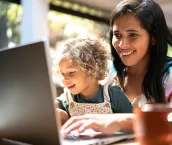 Mother using a laptop while holding her daughter at home