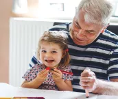 Cute little baby toddler girl and senior grandfather painting with colorful pencils at home. Grandchild and man having fun together