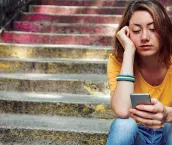 Teen girl dressed in yellow t-shirt sitting on stairs and is breaking up with her boyfriend through text messages.