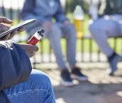 Close Up Of Teenagers With Mobile Phone Vaping and Drinking Alcohol In Park