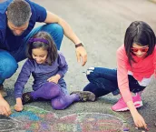 Father and his daughters are drawing butterfly with chalk.