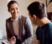 Happy psychologist talking to man with down syndrome while visiting him at home.