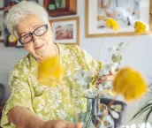 Senior woman arranging flowers in a vase at home.