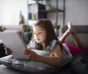 little girl laying on sofa at home and using digital tablet.