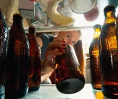 A young woman takes cold refreshing beer from out the fridge, inside view from fridge of hand holding the bottle.