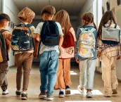 A group of schoolchildren with backpacks walk along the school corridor during recess.