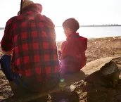 Fisherman and his grandson sitting on riverbank at sunset