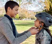 Shot of a young boy helping to secure his sister’s helmet before she rides her bicycle in the park
