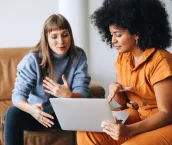 Two young businesswomen having a discussion while looking at a laptop screen. Two female entrepreneurs working as a team in a modern workplace.
