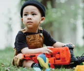 Image shows young toddler sitting in nature playing with toy truck Image shows young toddler sitting in nature playing with toy truck