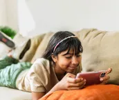 Young girl watching video (or playing mobile games) on mobile phone at home