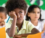 A photo of a young boy in a classroom and behind him are two young children blurred out in the background