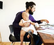 Young father working from home on his laptop with his baby in his lap