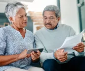 Shot of a mature couple using a mobile phone while going through paperwork together at home