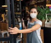 Happy business owner opening the door at a cafe wearing a facemask to avoid the spread of coronavirus Happy business owner opening the door at a cafe wearing a facemask to avoid the spread of coronavirus