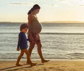 Pregnant mother exercising at the beach, holding her toddler's son hand by the sea, during sunset.