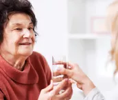 Home nurse helping a senior woman at home. She is giving a glass of water to her.