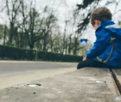 Sad boy in a blue jacket sitting alone on a wooden bench