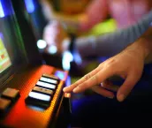 Closeup of unrecognizable man making money on slot machine in casino. He's playing slot poker. There are blurry people in background also playing.