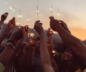 Group of friends holding burning sparklers against the sky
