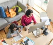 Young mother working on her computer with her daughters playing on their mobile devices