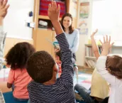 Elementary school kids raising hands to teacher, back view