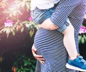 Pregnant woman with child. Mother and son on nature background, close-up. Child boy is sitting on belly of his mother, who pregnant for second time. Pregnancy, new life, family, parenthood concept.