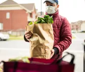 Mature man wearing protection mask, unloading grocery from car trunk