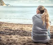 teenage girl sitting on beach looking out at the sea