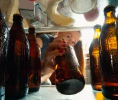 Young woman takes cold refreshing beer from out the fridge, inside view from fridge of hand holding the bottle.