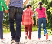 An image of a couple holding hands and two young children walking a dog.