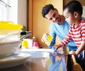 A young father doing dishes with his son