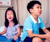 A photo of two children sitting on the floor. The boy who is older is sitting with his back to the younger girl and she is crying.