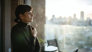 Young woman standing at a window at sunset contemplating at home