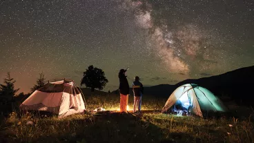 Mother and son tourists resting at camping in mountains at night sky full of stars and Milky way.