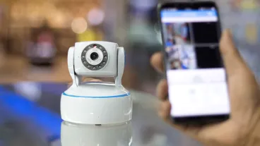 CCTV camera in the foreground and a hand holding a mobile phone in the background