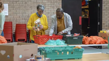 Group of volunteers organising food donations onto tables at a food bank in the North East of England. They are working together, setting up sections of the room in a church. Group of volunteers organising food donations onto tables at a food bank in the North East of England. They are working together, setting up sections of the room in a church.
