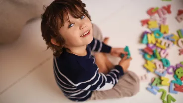 Young child sitting on the floor playing with wooden alphabet letters.