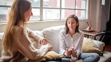 Mother and teenage daughter sitting on the sofa having a talk at home