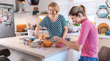 A young woman with hearing aids talking to her mother in the kitchen. They have a breakfast and enjoying the time they spending together. A young woman with hearing aids talking to her mother in the kitchen. They have a breakfast and enjoying the time they spending together.