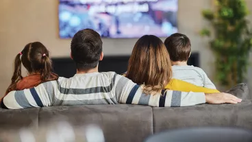 Rear view of relaxed family watching TV on sofa in the living room.