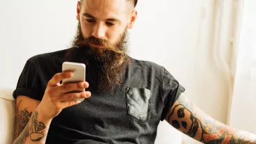 Young bearded tattooed man using mobile phone.