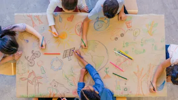 An aerial view of a multi ethnic group of children learn about going green and color in environmentally friendly concepts surrounding a drawing of Earth.