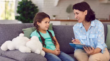 Smiling little girl talks to a cheerful child psychotherapist during a therapy session in the office.