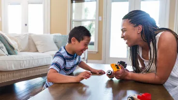The young boy with Down Syndrome enjoys play therapy with his therapist at home.