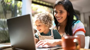 Mother using a laptop while holding her daughter at home