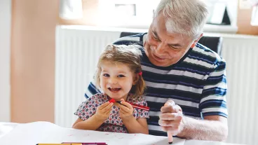 Cute little baby toddler girl and senior grandfather painting with colorful pencils at home. Grandchild and man having fun together