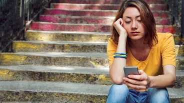 Teen girl dressed in yellow t-shirt sitting on stairs and is breaking up with her boyfriend through text messages.